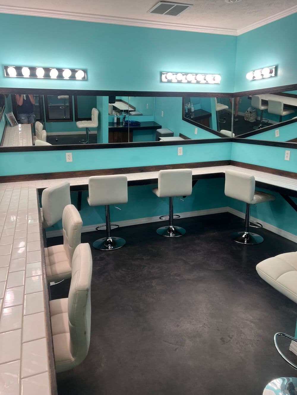 Modern salon interior featuring turquoise walls, white bar stools, and bright vanity mirrors.