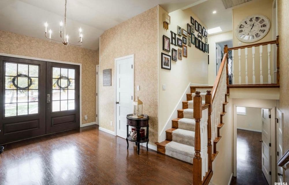 Bright entryway with dark double doors, wooden staircase, and wall of framed pictures.