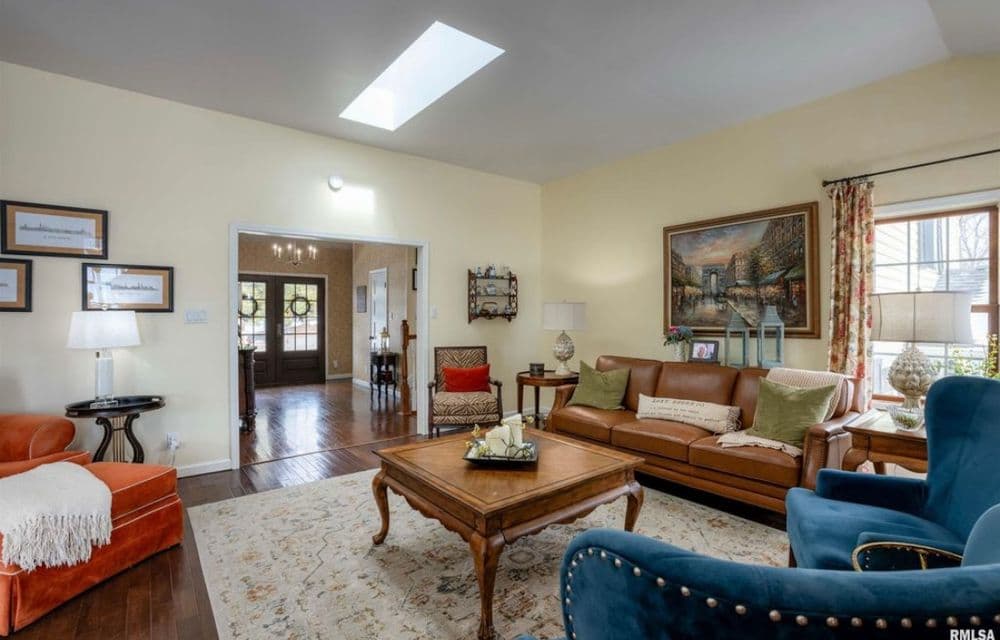 Cozy living room with a leather sofa, blue armchair, and artwork, featuring natural light from skylight.