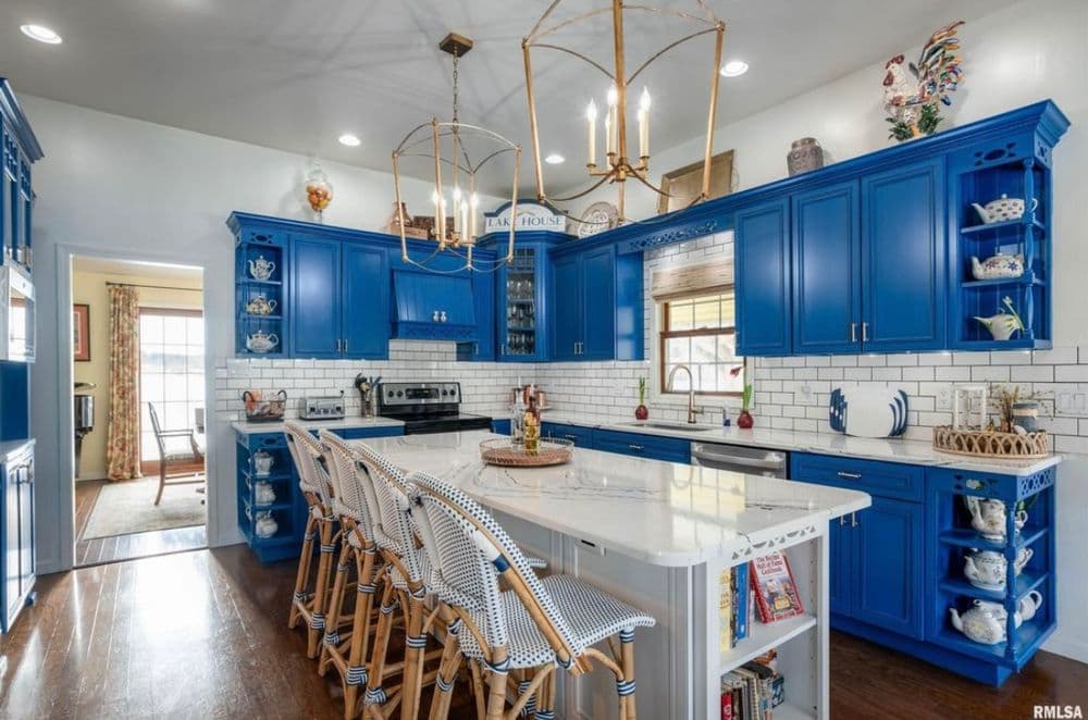 Bright blue kitchen with white countertops, bar seating, and elegant lighting fixtures.