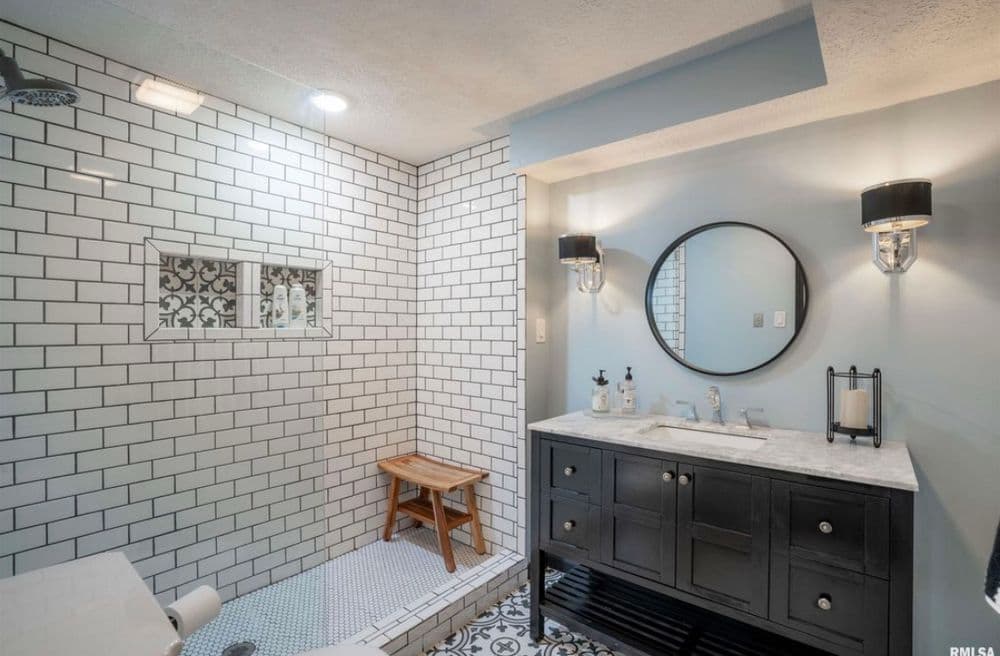 Modern bathroom featuring white subway tiles, round mirror, dark vanity, and patterned floor.