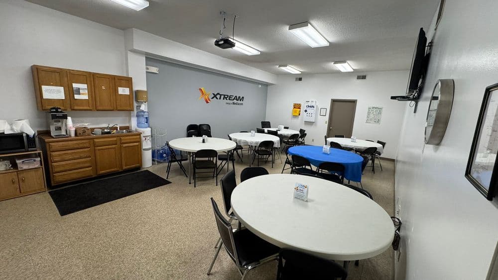 Bright and spacious break room with round tables, kitchen area, and Xtream branding on the wall.