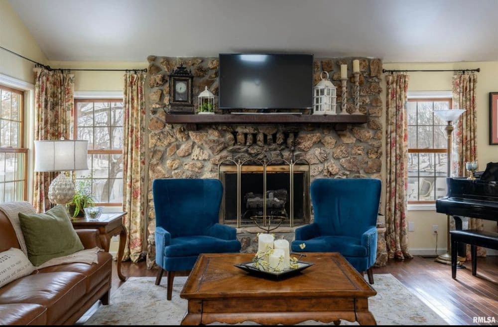 Cozy living room with stone fireplace, blue armchairs, and elegant decor accents.