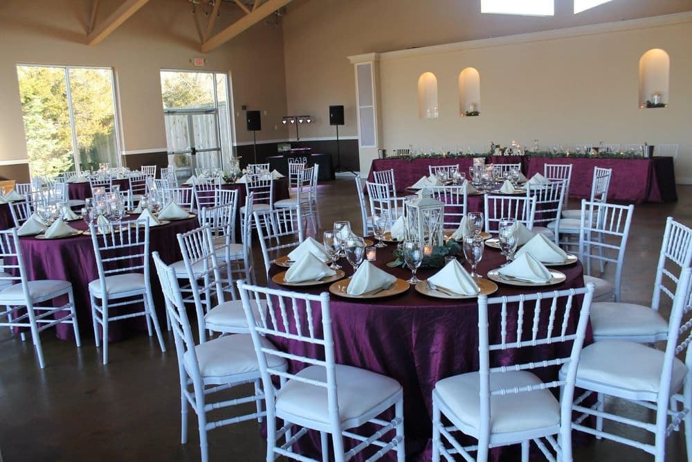 Elegant wedding reception setup with round tables, white chairs, and detailed place settings.