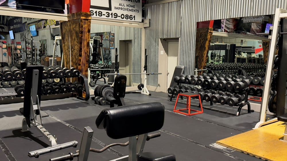 Gym interior with weightlifting equipment, benches, and dumbbells for strength training.