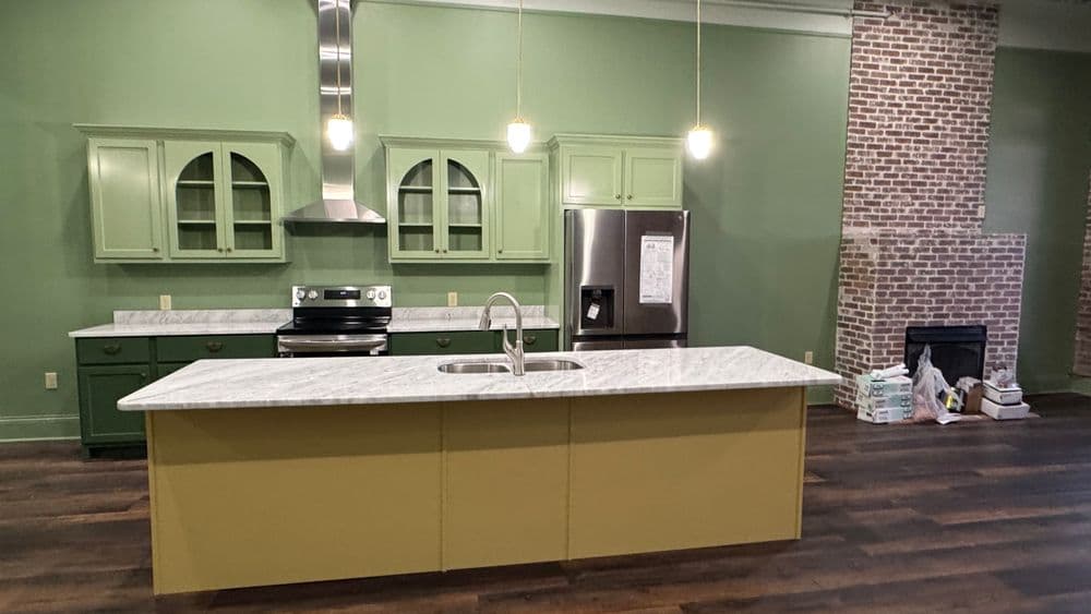 Modern kitchen with green cabinets, marble countertops, and a brick fireplace accent wall.