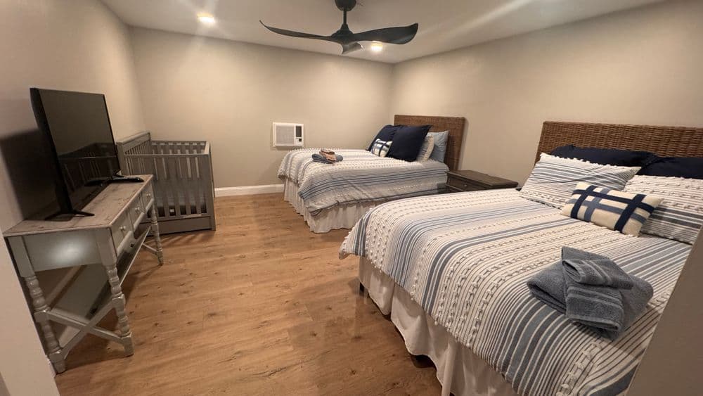 Cozy bedroom with two beds, TV, crib, and modern decor, ideal for family stays.