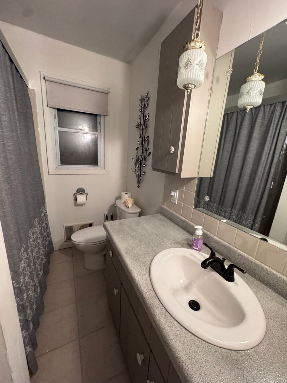 Modern bathroom with gray cabinets, sink, toilet, and decorative curtains. Clean and functional design.