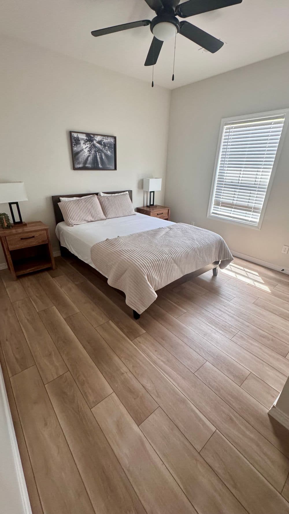 Modern bedroom with a queen bed, wooden nightstands, and natural light from a window.