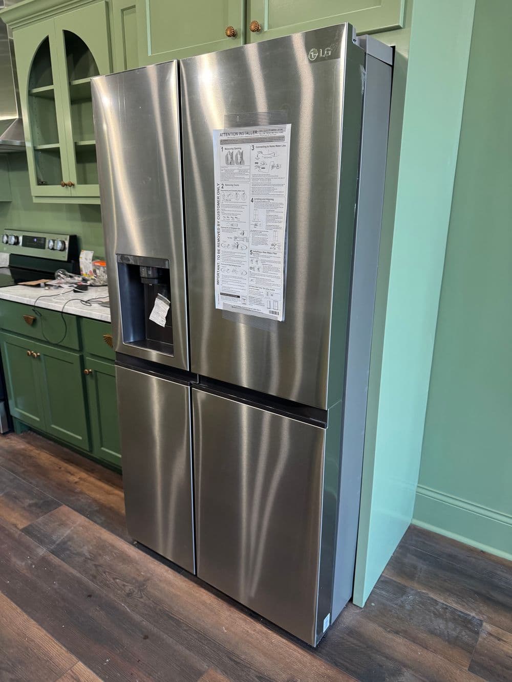 Stainless steel LG refrigerator in modern kitchen with teal cabinetry and wood floor.