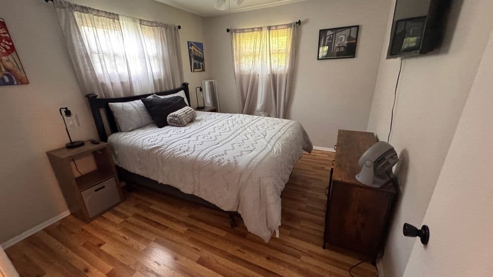 Cozy bedroom featuring a queen bed, wooden furniture, and natural light from large windows.