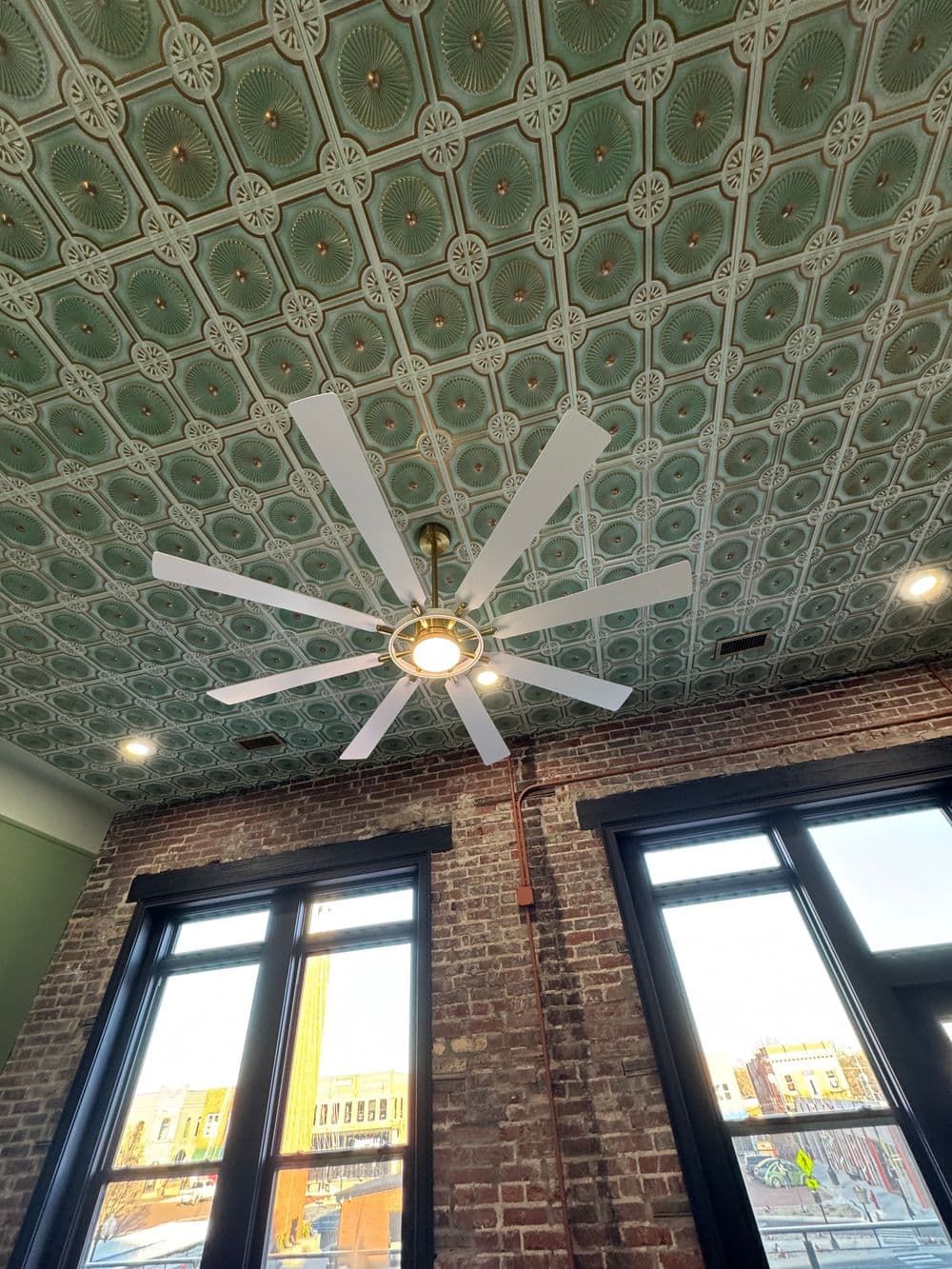 Modern ceiling fan with white blades in a brick-walled room with a vintage green patterned ceiling.
