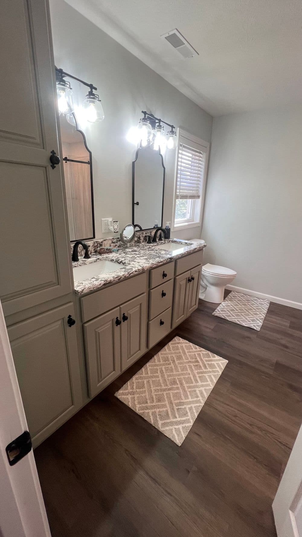 Modern bathroom interior with double vanity, granite countertop, and stylish rugs on wooden floor.