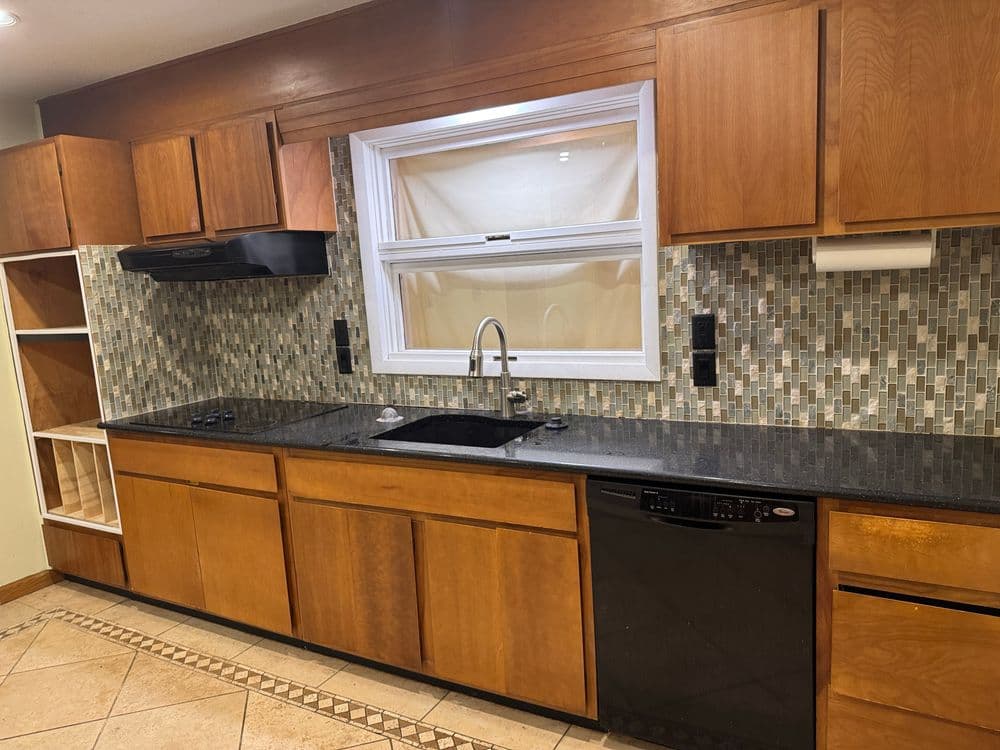 Modern kitchen with wooden cabinets, black granite countertops, and mosaic backsplash tiles.
