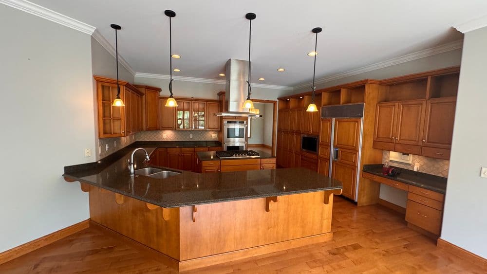 Modern kitchen with wood cabinetry, granite countertops, and pendant lighting. Open layout design.