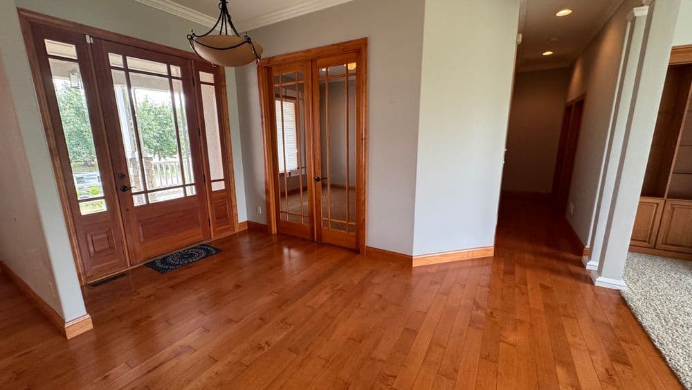 Spacious entryway with hardwood floors, glass doors, and natural light, leading to hallways.