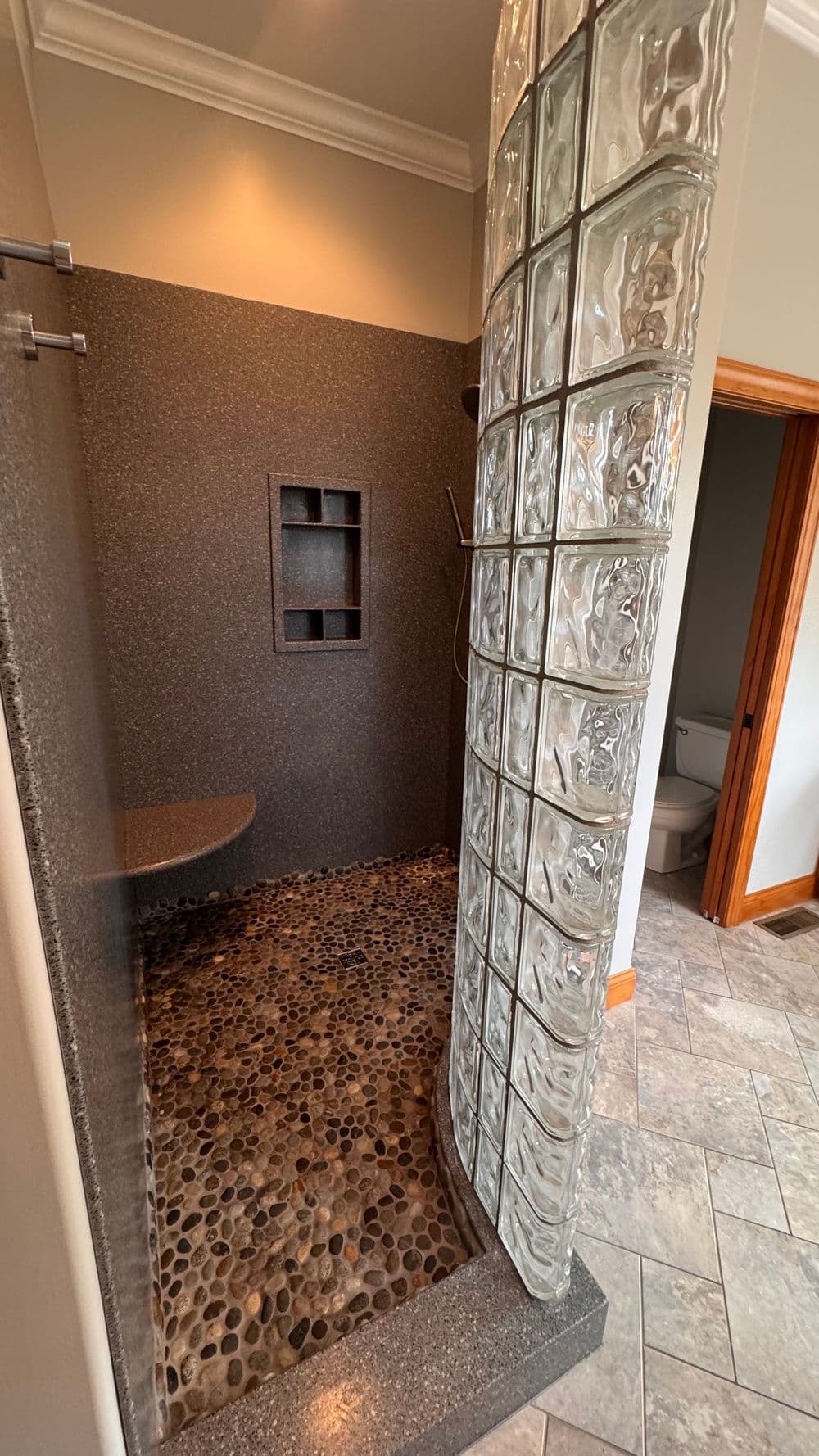 Modern walk-in shower with glass block wall and pebble floor design. Elegant bathroom decor.
