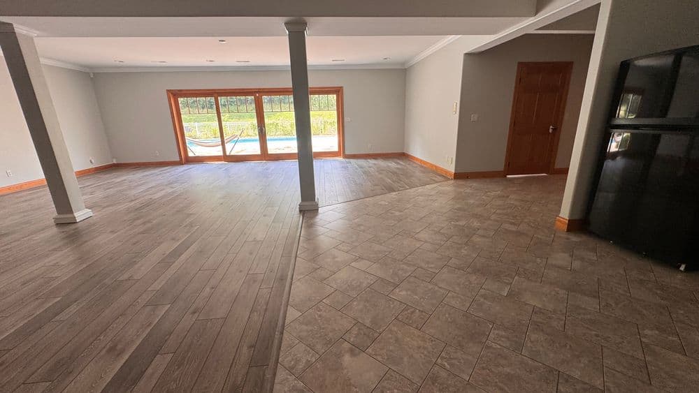 Spacious open living area with tile and wood flooring, large windows overlooking a pool.