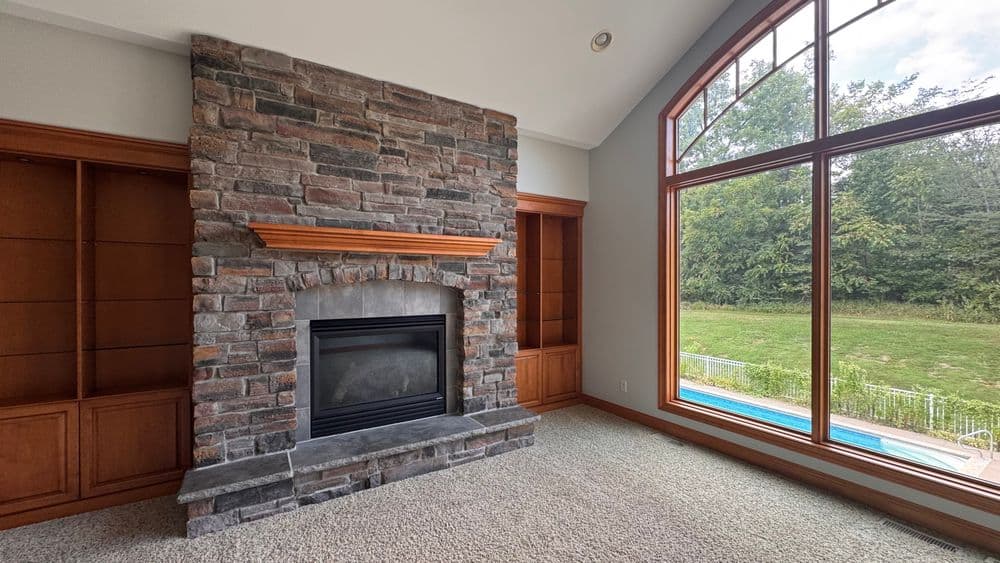 Modern living room with stone fireplace, built-in shelves, and large windows overlooking pool.
